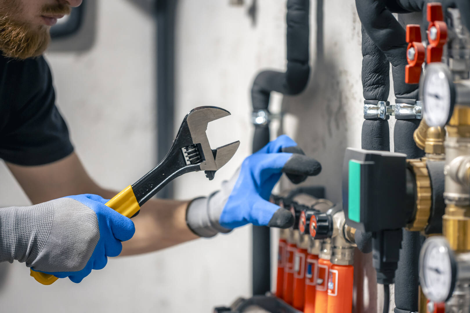 A man installs a heating system in a house and checks the pipes with a wrench.